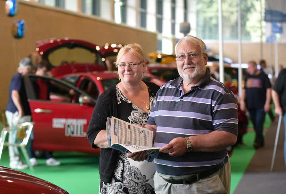 Female and male couple at car show smiling and holding the event guide